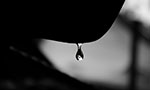 Foto em preto e branco de uma gota se desprendendo de uma superfície.
