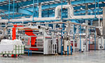 Foto de um pátio industrial, com equipamentos e tubos de ar metálicos, teto alto e chão de linóleo.