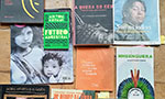 Foto vários livros dispostos como uma colagem. Os títulos: “A terra dos mil povos”; “Futuro Ancestral”; “A queda do céu”, na capa o rosto pintado de uma pessoa indígna; revista “História - Biblioteca Nacional” com a manchete “Somos índios” e a foto de um homem indígena; outra revista com uma mulher indígena segurando uma criança; “Os povos indígenas frente ao direito autoral e de imagem”, “Nheenguera”, na capa um cocar com plumas azuis/verdes; “Índios na visão dos índios”, na capa o rosto de uma pessoa indígena; “Os donos da terra”, na capa uma pessoa indígena com as mãos na cintura e de frente para um trator de construção; e “Ailton Krenak”.