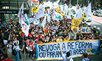 Foto de um protesto. Pessoas jovens ocupam duas faixas da Av. Paulista ao lado da estação Trianon-Masp. Elas seguram bandeiras e na frente levam um cartaz dizendo "Revoga a reforma ou paramos o Brasil".