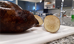 Foto de uma batata yacon sobre uma mesa de laboratório. Do lado, um pedaço cortado mostrando a parte interna do yacon.