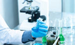 Fotografia de uma mão segurando um frasco em um laboratório, que pode ser visto ao fundo.