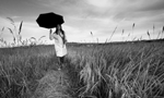 Mulher, vestida com jaleco, segurando uma prancheta e um guarda-chuva enquanto caminha sobre um campo gramado.