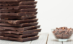 Tigela com pedaços de chocolate sobre uma superfície de madeira, ao lado de vários tabletes de chocolate.