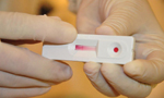 Duas mãos com luvas segurando um teste rápido de hepatite.