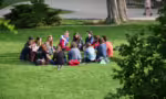 Fotografia de jovens adultos sentados em roda em um gramado, conversando