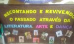 Fotografia de um painel marrom com o título "Recontando e Revivendo o Passado através da Literatura, Arte e Dança" nas cores amarela, azul, roxo e rosa. Abaixo o título, tem impressões de capas de livros infantis que remetem ao título