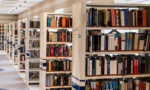 Fotografia de um corredor claro de uma biblioteca com diversas estantes com livros.