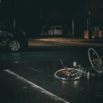 Fotografia de uma rua escura com um carro batido e uma bicicleta caída no chão